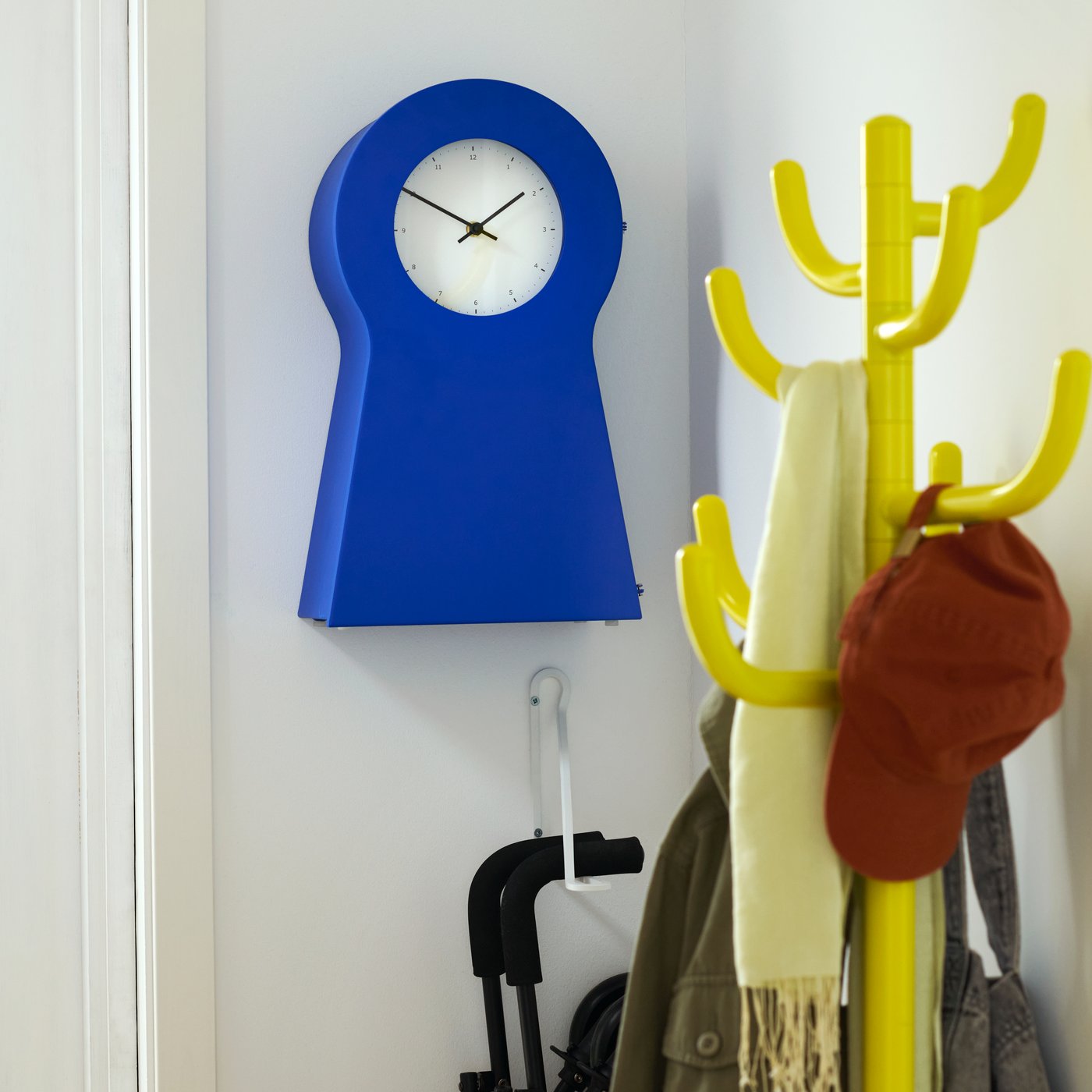 Hoek in de hal met BONDSKÄRET kapstok in geel met daarachter aan de muur de blauwe IKEA PS 1995 klok.