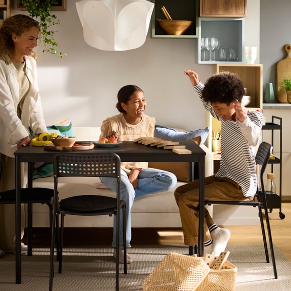 Two laughing children are sitting at a black SANDSBERG table in a sunlit dining area, playing a game together.