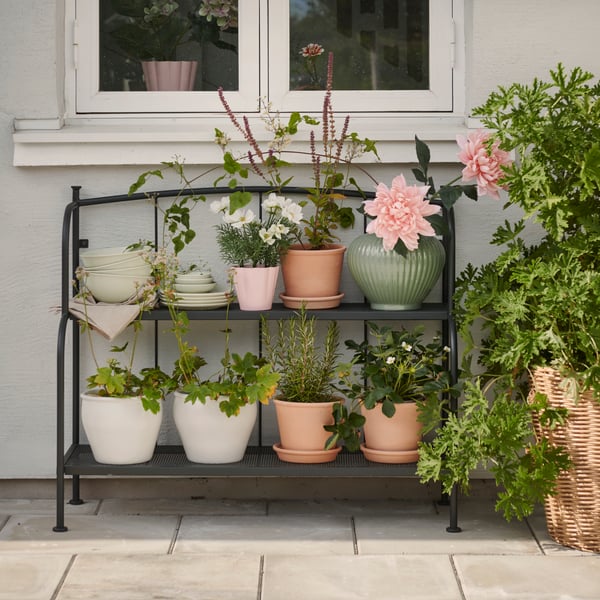 A patio with a grey LÄCKÖ shelving unit made for outdoor use, displaying various potted plants and flowers.