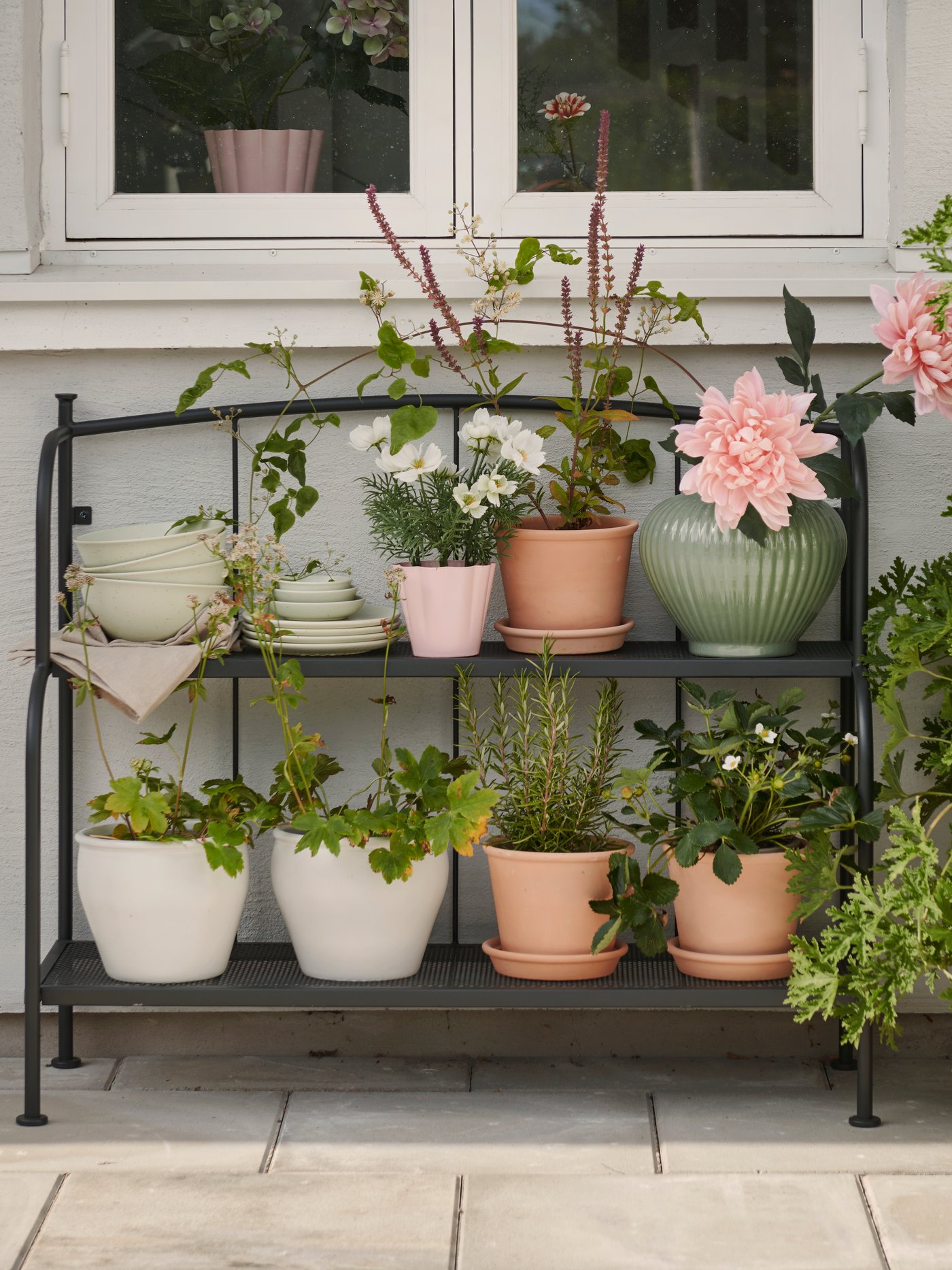 A patio with a grey LÄCKÖ shelving unit made for outdoor use, displaying various potted plants and flowers.
