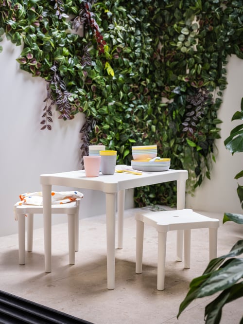 An outdoor area with KALAS mugs alongside KALAS plates, placed on a children's table and surrounded by children's stools.