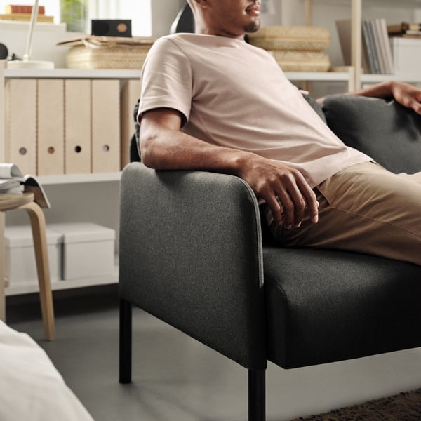 Ein Mann sitzt auf einem GLOSTAD 2-Sitzer-Sofa in Knisa dunkelgraues im Wohnzimmer