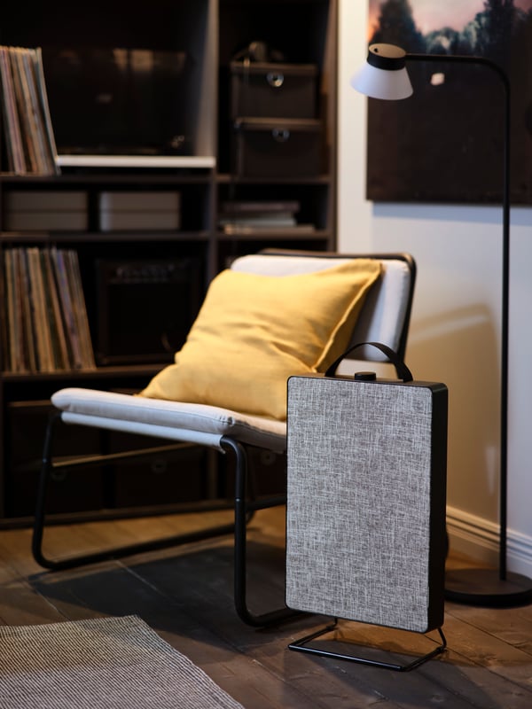 A black, rectangular FÖRNUFTIG air purifier with a handle stands on the floor by a rug and a low, light grey easy chair.