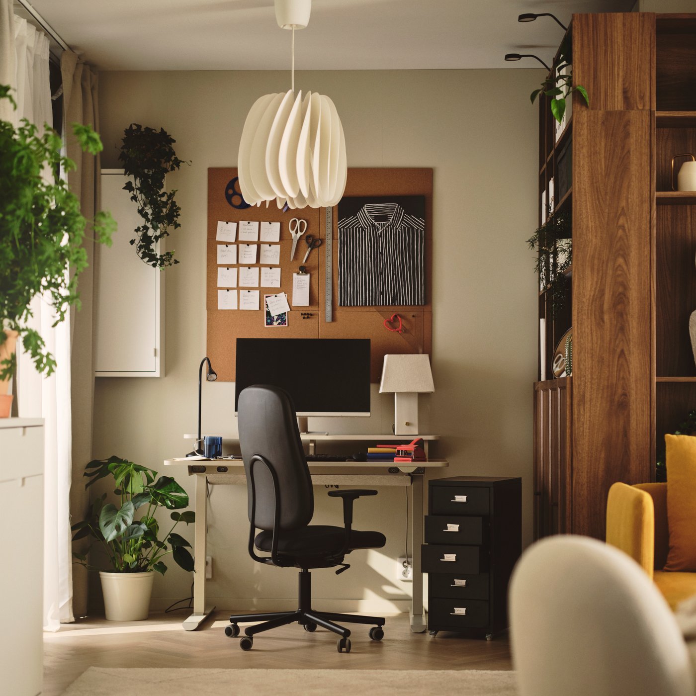 An office with a dark grey SMÖRKULL office chair with armrests beside a desk and plants near a wall.