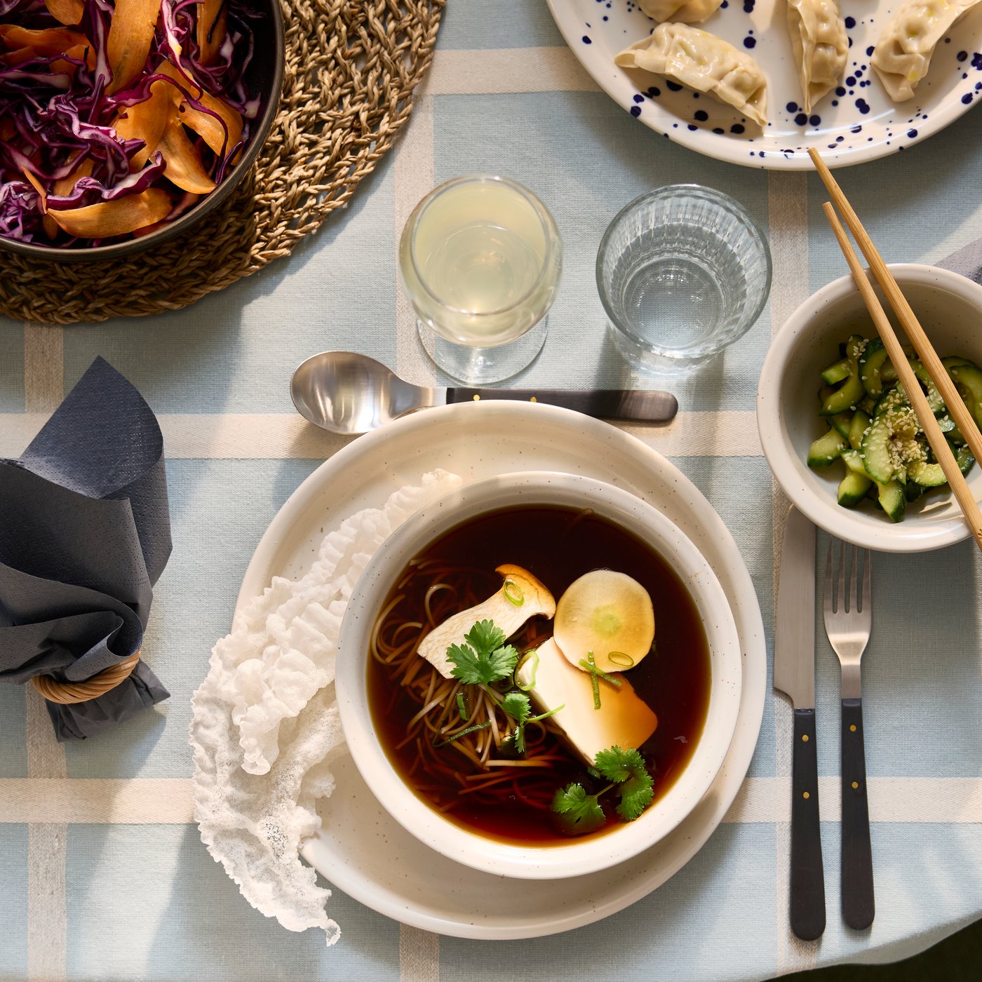 A dotted/light beige DAGGASTER plate and bowl has a soup made of mushrooms, tofu and noodles, next to a bowl of avocados.