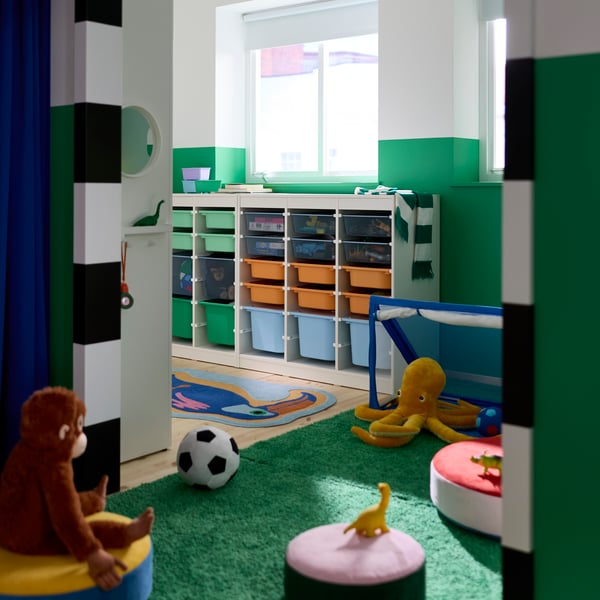 A children’s bedroom with walls painted green and white and a TROFAST system with boxes in different sizes and colours.