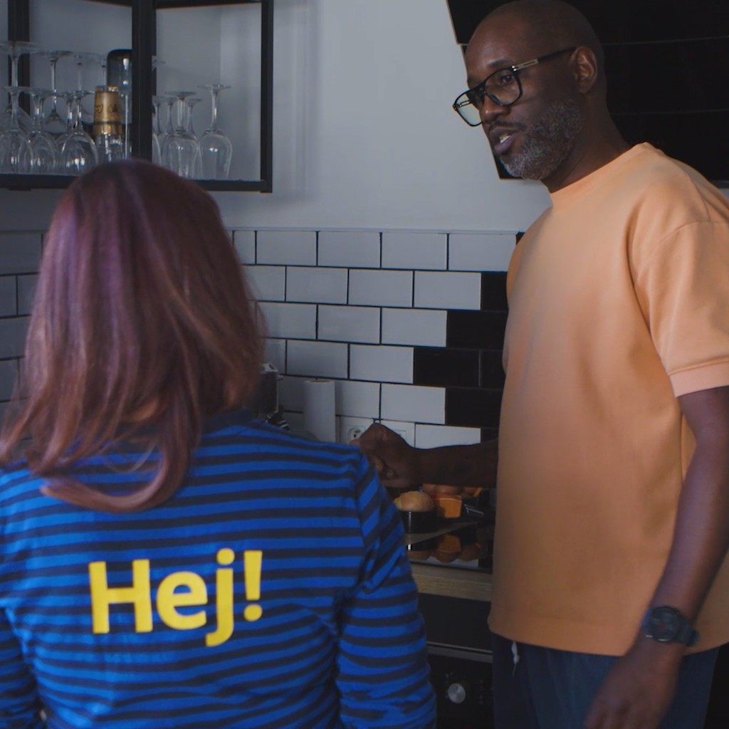 Collaboratrice IKEA de dos parlant à un client portant des lunettes et un t-shirt orangé