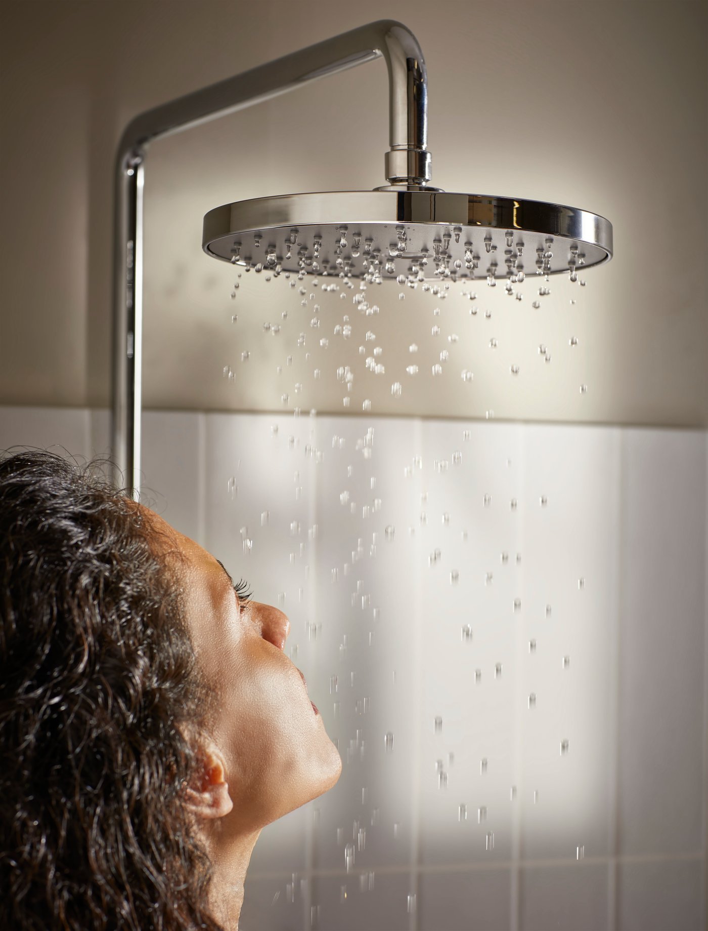 A woman looking at he shower with water dripping down in front of white tiles
