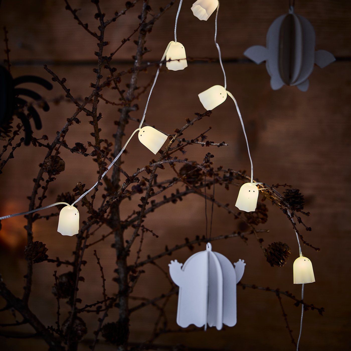 A white ghost-shaped KUSTFYR hanging decoration hung on branch with a KUSTFYR ghost LED lighting chain.