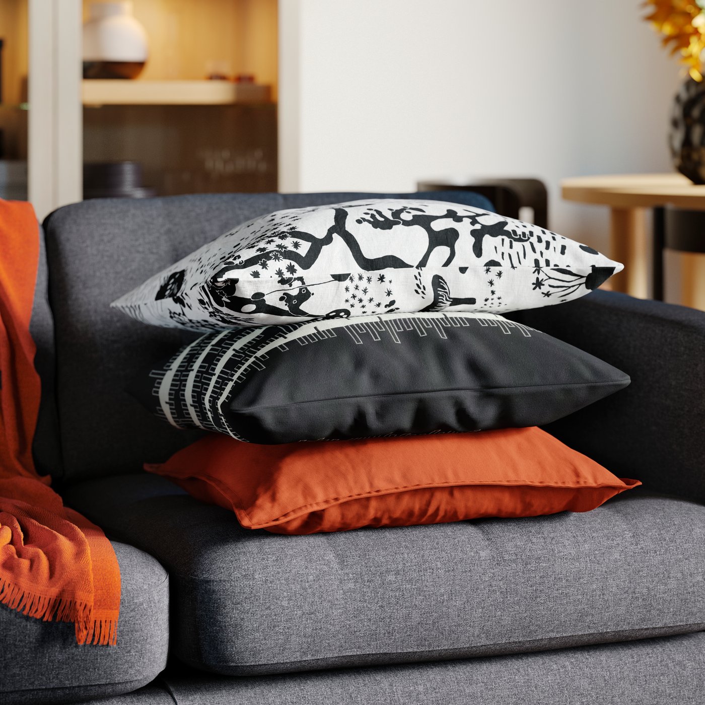 A pile of three cushions sits on top of a dark grey 2-seat sofa in an Instagram worthy living room.