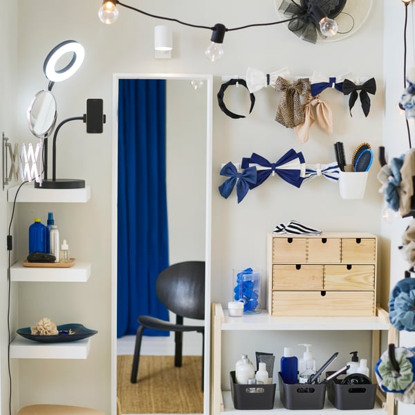 A pine MOPPE mini chest on a white shelf with hair acessories around it. A white NISSEDAL mirror is on the wall beside it.