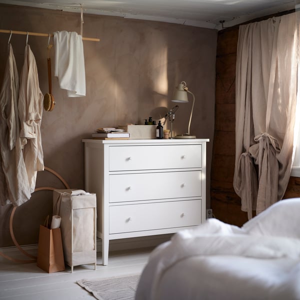 Bolsa para ropa PURRPINGLA en color beige con soporte de 42 litros, colocada junto a una cómoda en una recámara de estilo cálido.