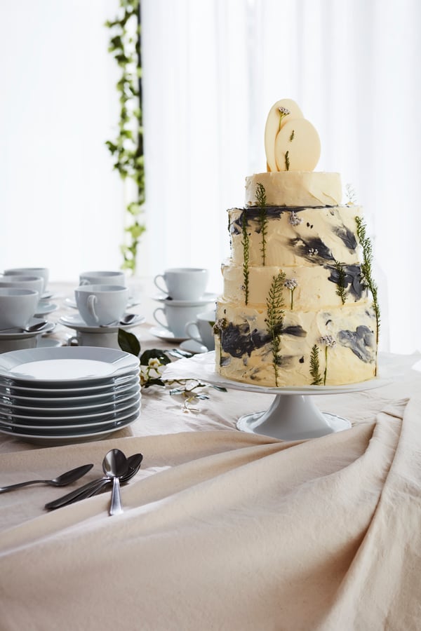 A large wedding cake sits next to several plates ready to serve. The cake is place on a white cake stand.