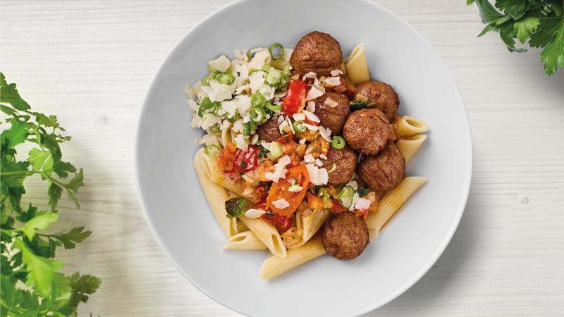 Penne & Fleischlosbällchen  mit Gemüseragout, Parmesan und Frühlingszwiebeln auf einem Teller präsentiert