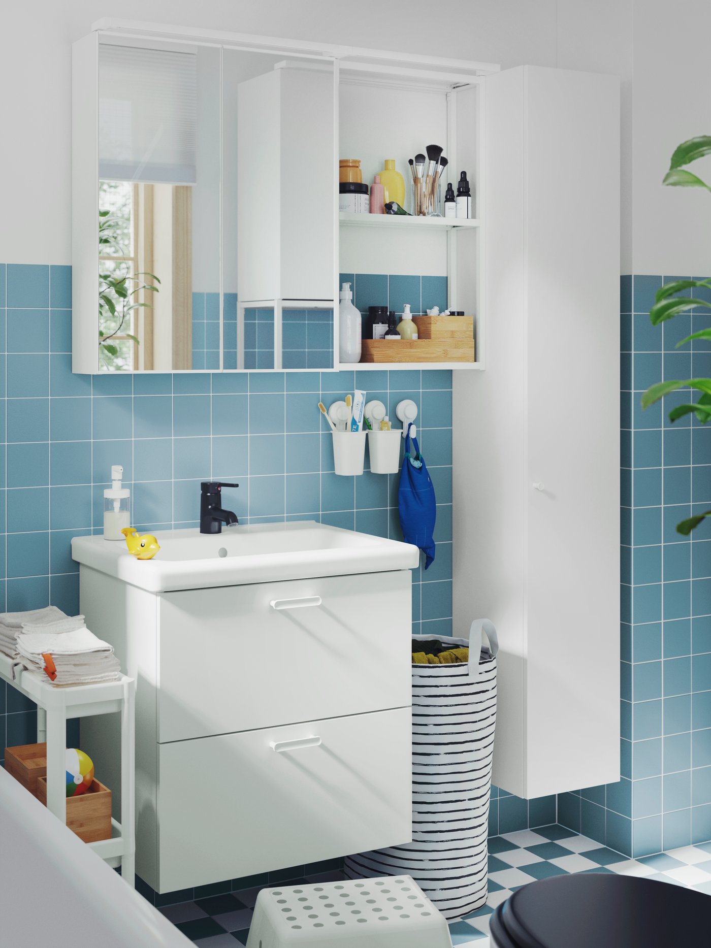 A small, blue-tiled bathroom has a white ENHET wash-stand, a mirror cabinet, a high cabinet and a white VESKEN trolley.