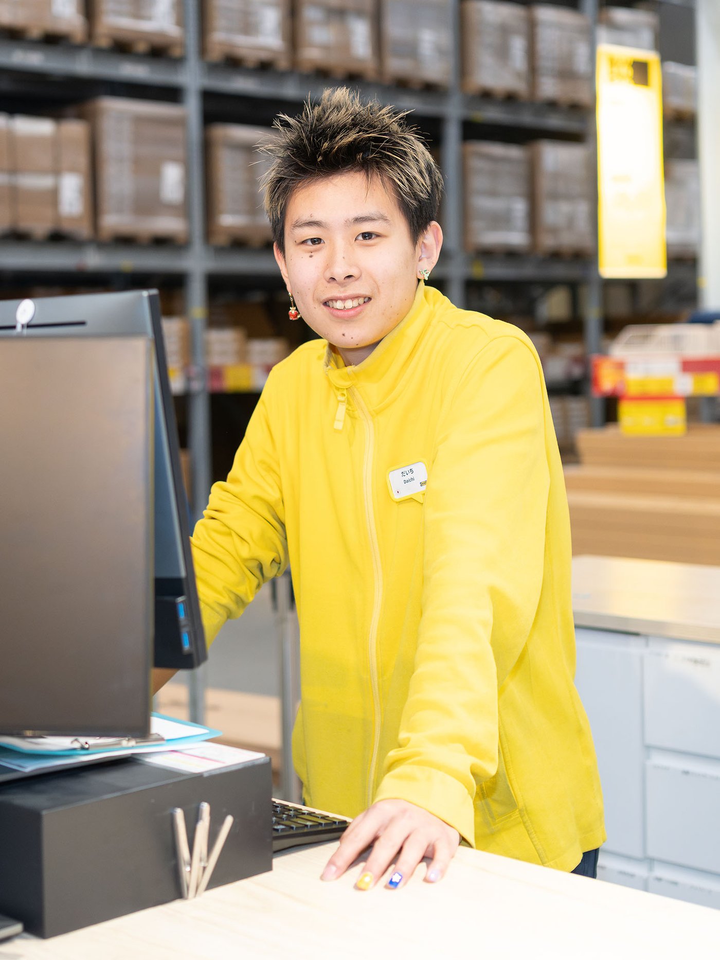 セルフサービスエリアのカウンターで、黄色いユニフォームのイケアのコワーカーがモニター横に立っている