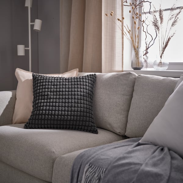 Funda de cojín SVARTPOPPEL en color carbón colocada sobre un sofá en una sala.