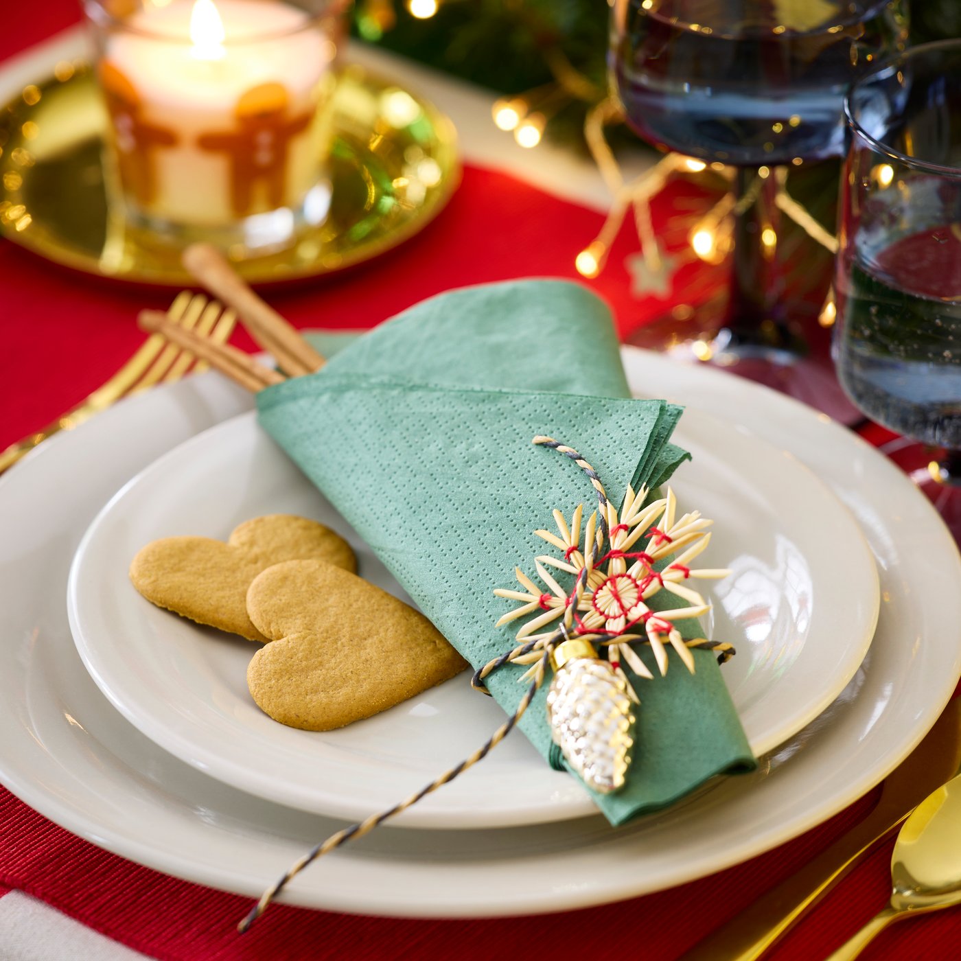 White IKEA 365+ plates stacked with blue napkin folded on top. Cookies on plate with festive decorations behind