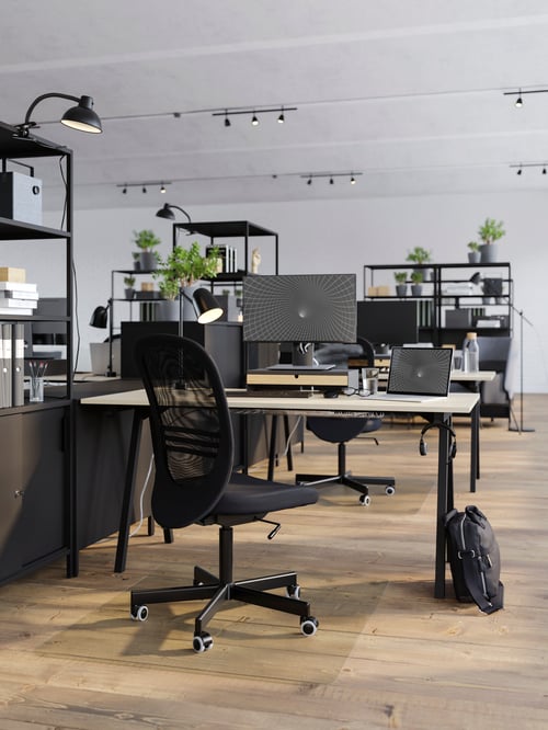 A TROTTEN desk and black FLINTAN chair in a light open plan office that's divided up with open shelving and cabinets.