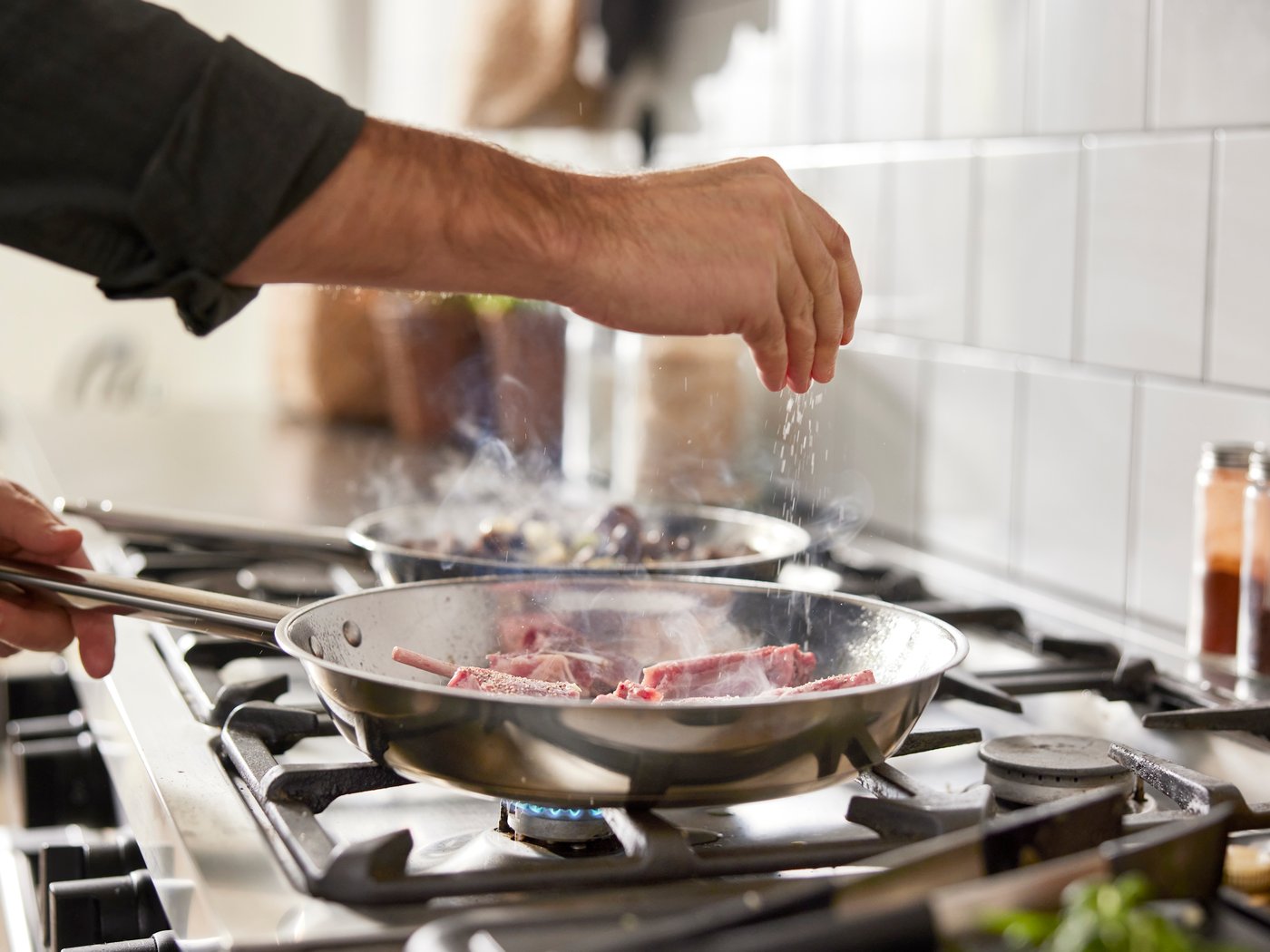 En mann salter kjøtt i en IKEA 365+ stekepanne på komfyren.