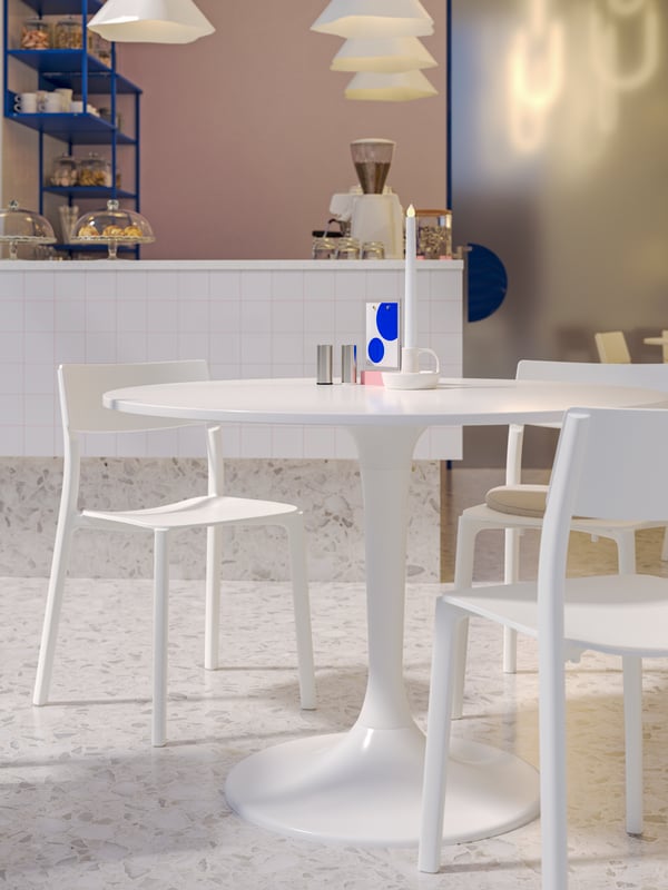 A white DOCKSTA table and white JANINGE chairs next to a café bar with serveware on blue PLATSA open shelving units.
