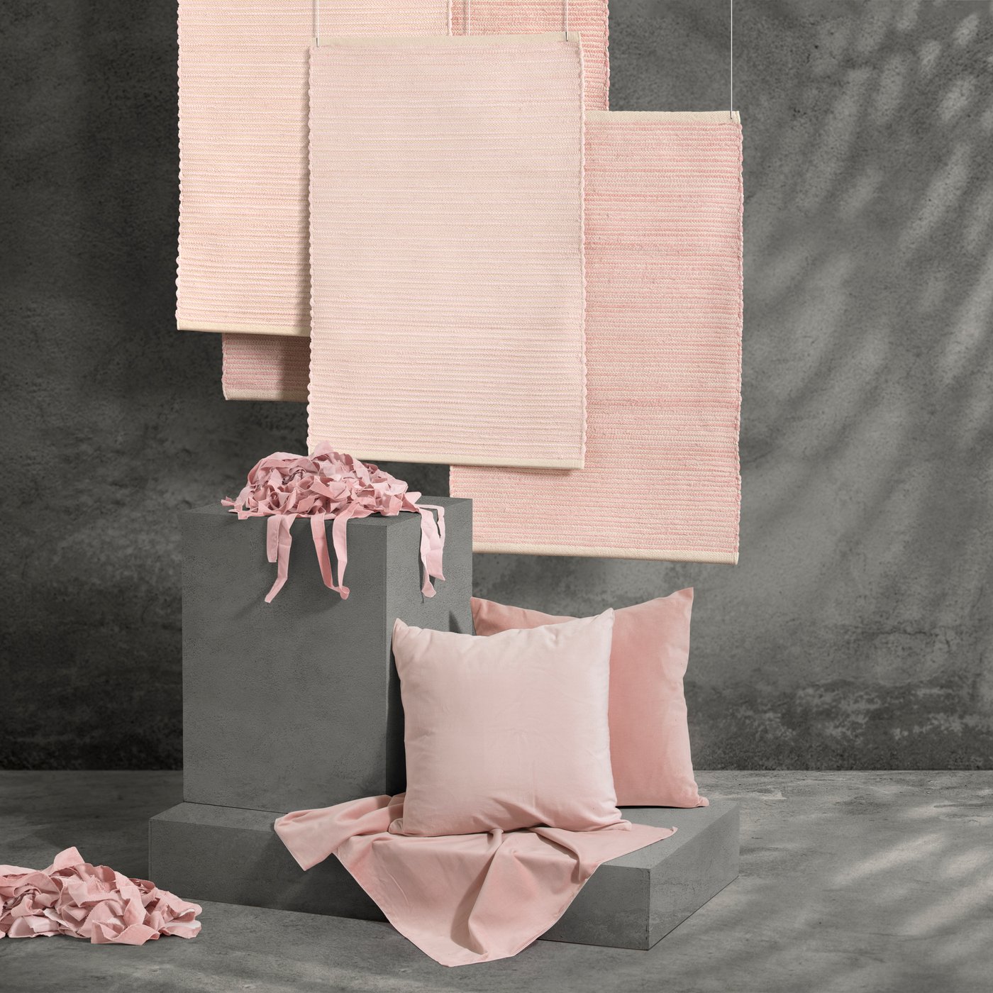 La serie SANELA con biancheria da letto rosa e tappeti esposta in un ambiente con pavimento e sfondo grigio.