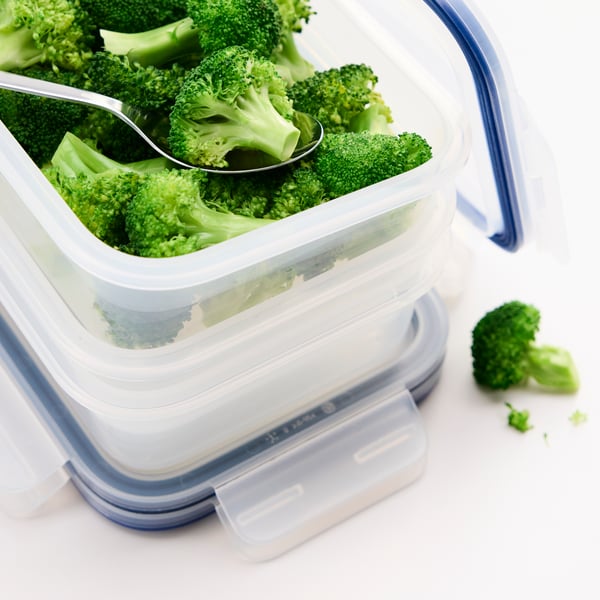 Close-up of a stack of IKEA 365+ plastic food containers. The open container on top holds pieces of broccoli and a spoon.