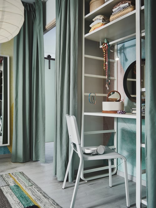 A green room with an ELVARLI shelf unit being used as dressing table with TIBAST curtains used as a door pulled to one side.