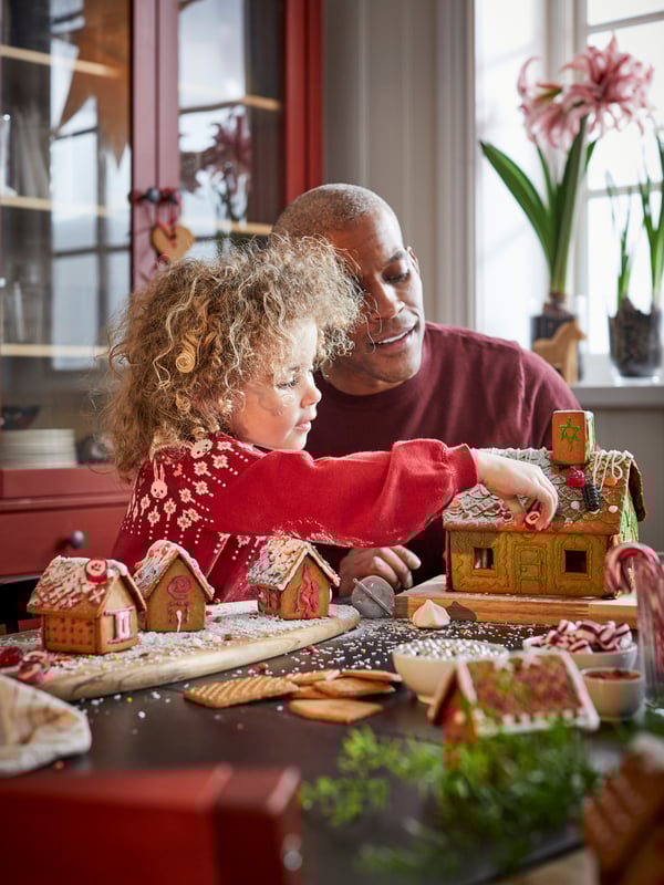 Young girl and Father decorating traditional Swedish VINTERSAGA gingerbread houses at Christmas.