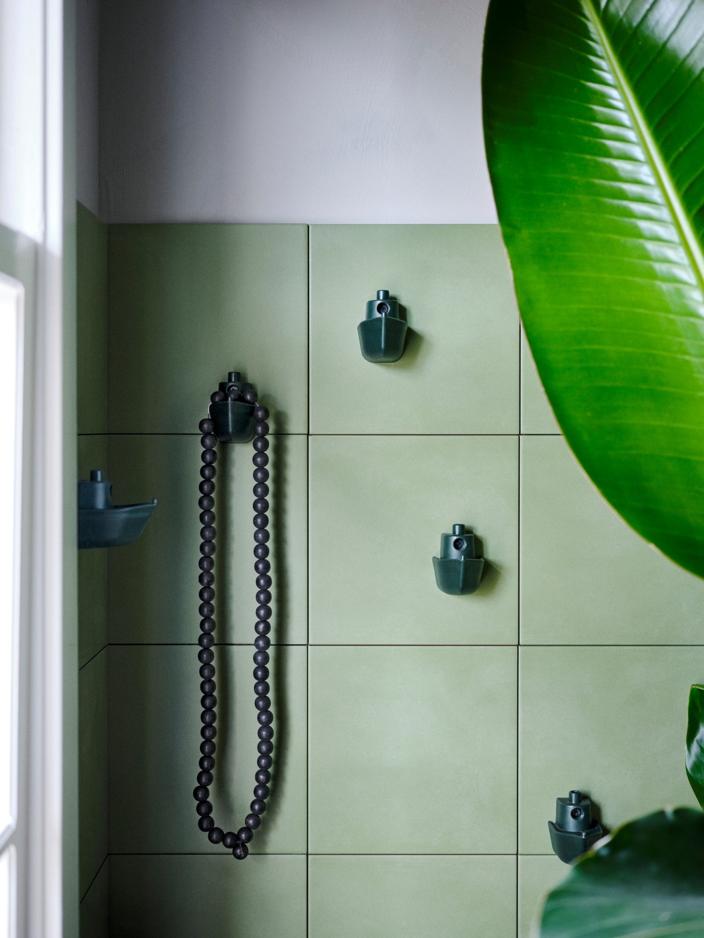 Quatre crochets verts KNOPARE en forme de bateau sont suspendus à des tuiles vert olive dans une salle de bains.