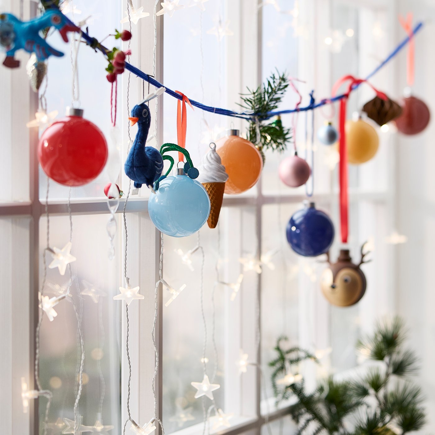 Assorted VINTERFINT tree decorations hanging from a blue string across a window adding a festive touch to a room.