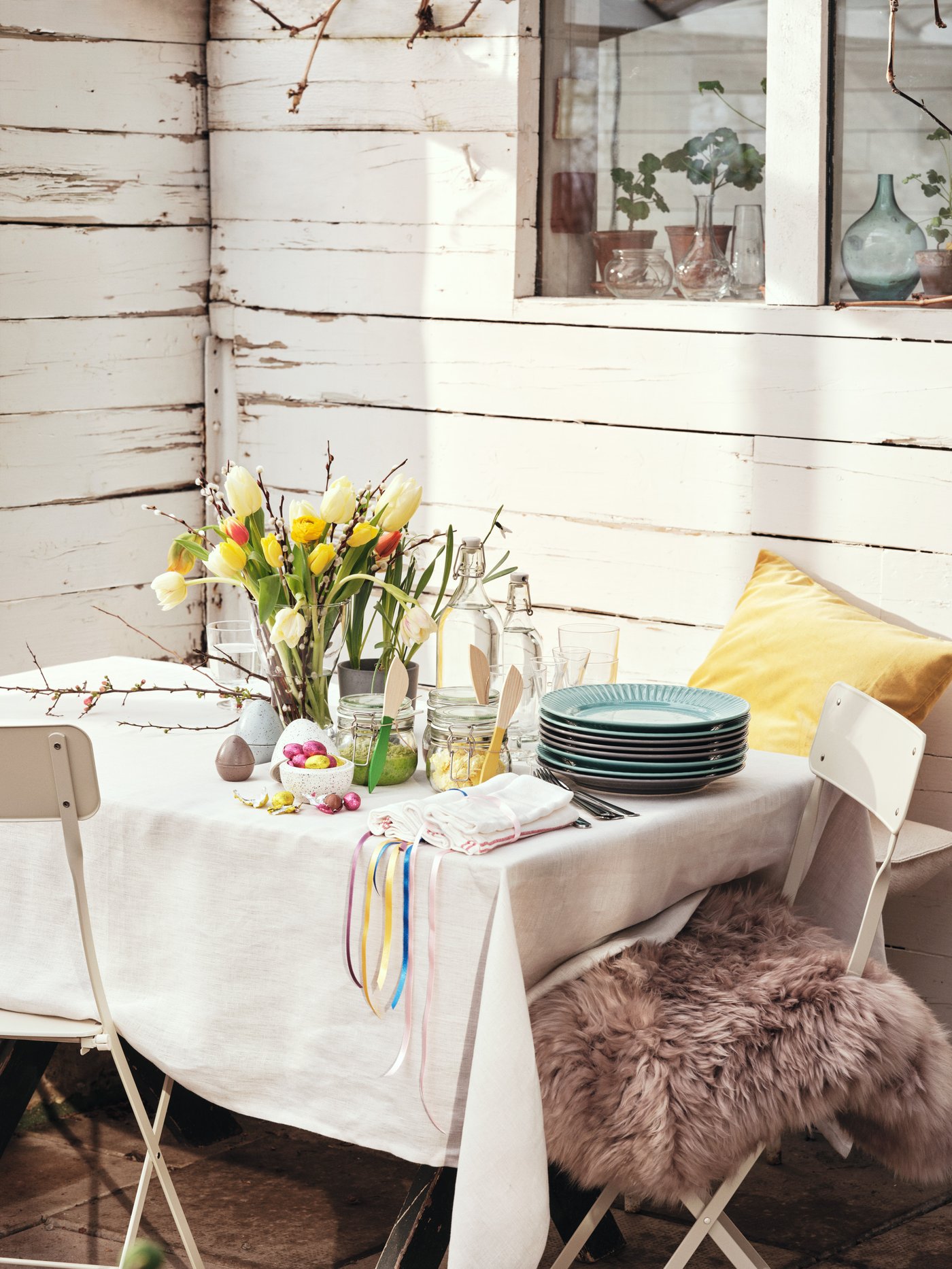 Et havebord på en terrasse dækket med en lys dug og påskeliljer.