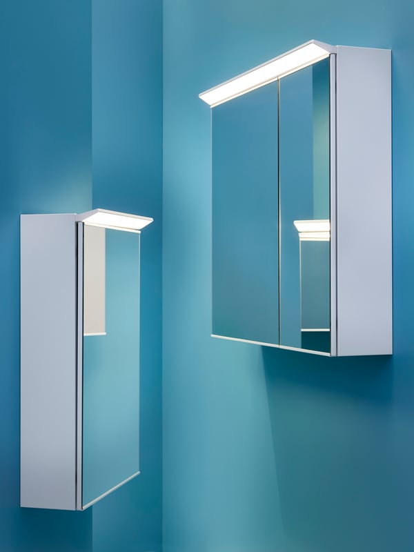 Two lit-up TREASJÖN mirror cabinets, in different sizes, are facing each other in a teal-colored space.