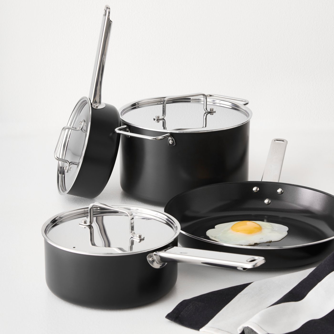 Un comptoir blanc où est posée une batterie de cuisine GULDÖRING de sept pièces, dont des casseroles et une poêle à frire antiadhésives en acier inoxydable.