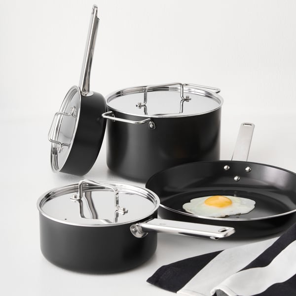 A white countertop with a black-grey GULDÖRING 7-piece cookware set, featuring non-stick stainless steel pots and frying pan