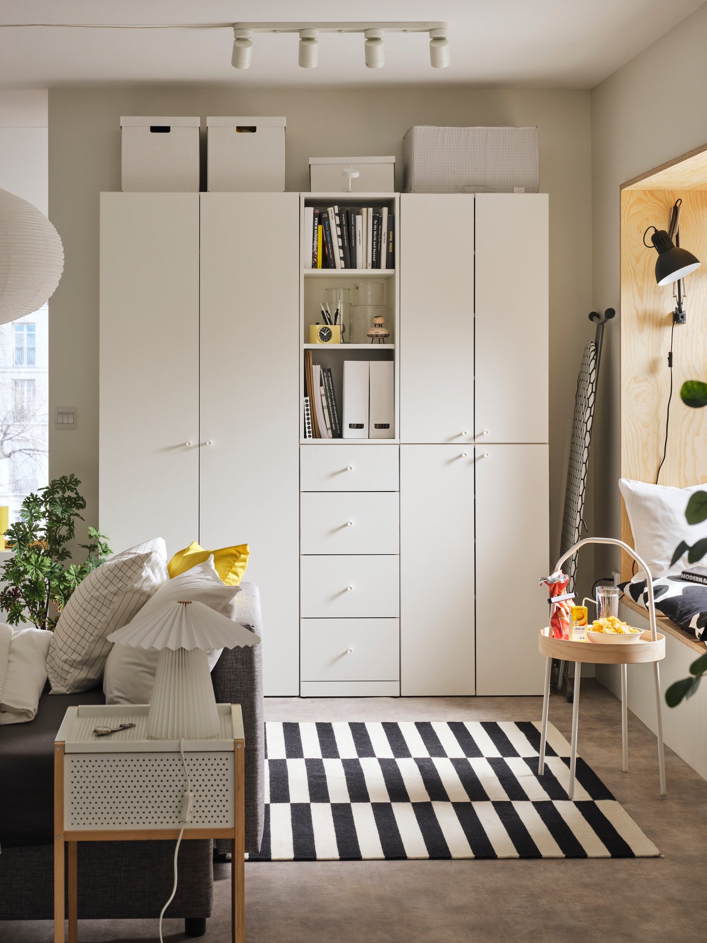 A living space with a LASTARE wardrobe combination alongside a sofa, indoor plants and a black-and-white striped rug.