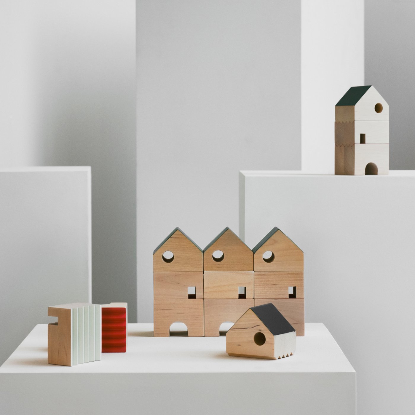 A light space with five FÄLTLÖNN three-part, solid-wood decorative houses artfully arranged on white boxes.
