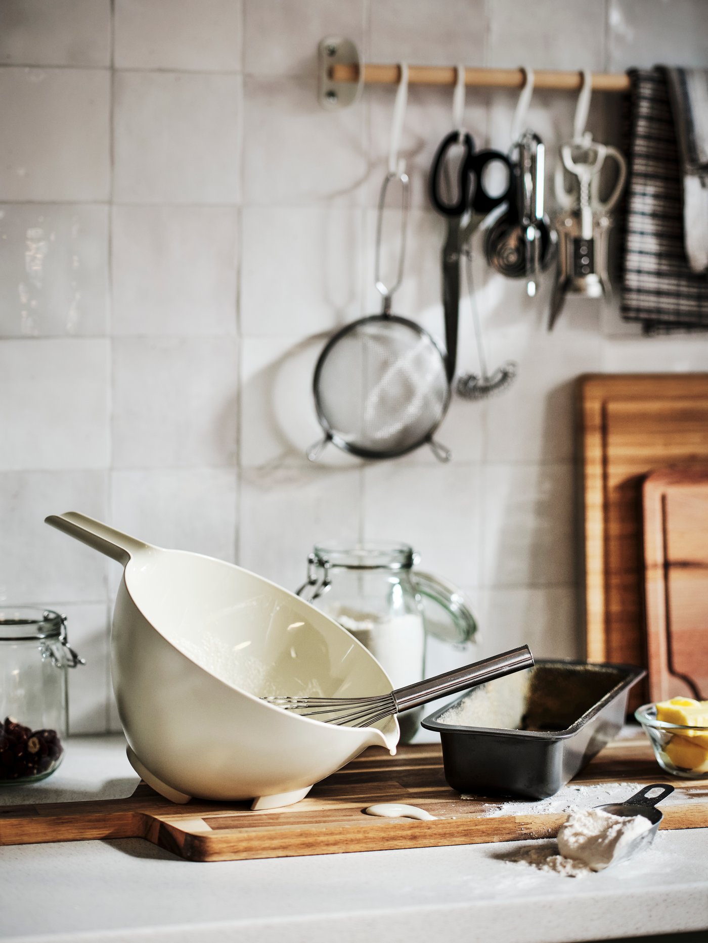 Un piano di lavoro di una cucina con vari strumenti e utensili, tra cui una ciotola beige VISPNING, fruste, e altri oggetti appesi.