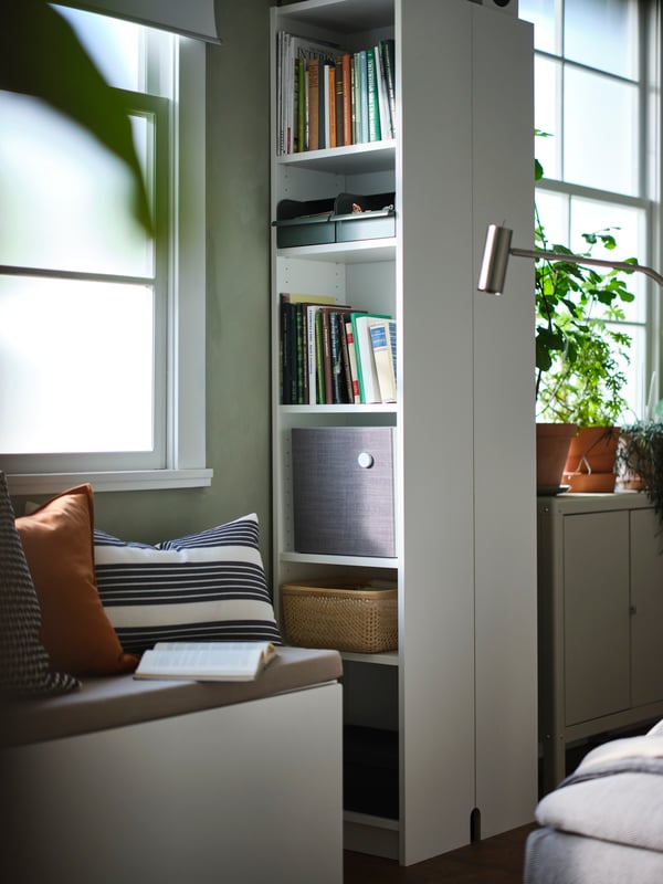 A SMÅSTAD bench with toy storage in front of two back-to-back white BILLY bookcases holding books, a speaker and small boxes.