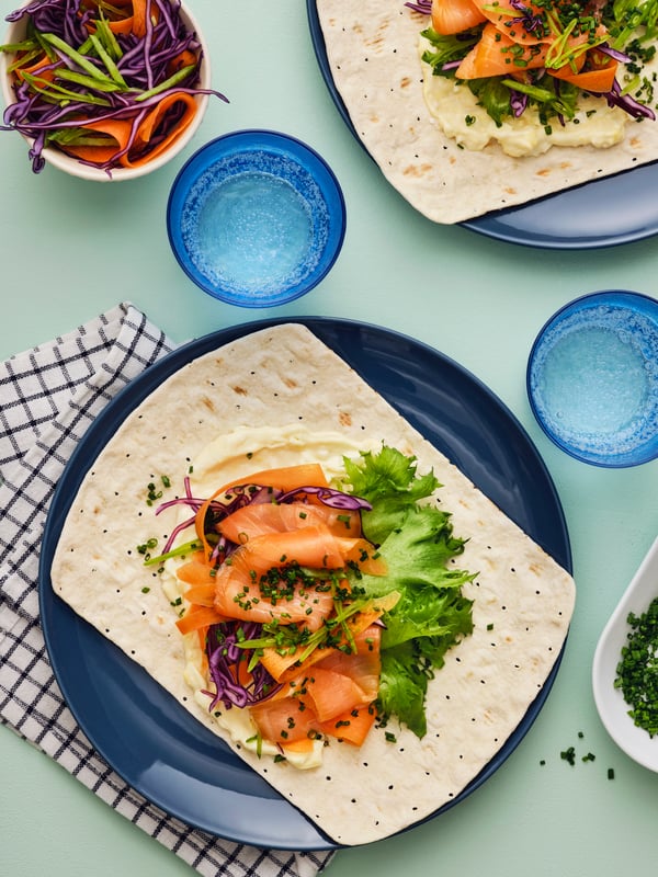 A TUNNBRÖD soft artic thinbread with lettuce, red cabbage and pieces of SJÖRAPPORT cured salmon is served on a blue plate.