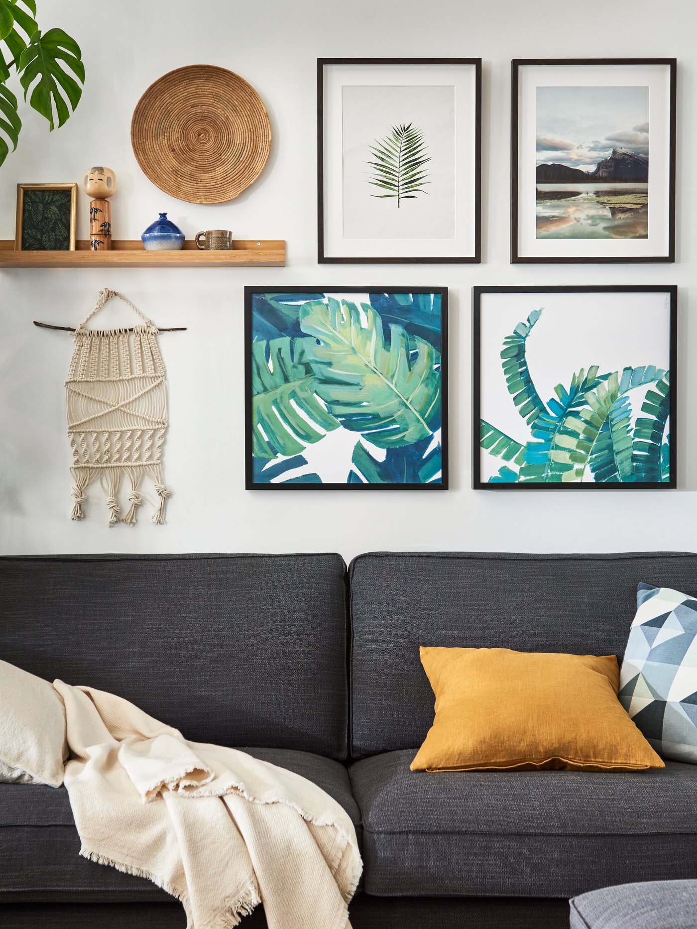 Dvoumístná pohovka KIVIK v antracitové barvě pod domácí obrazovou galerií tvořenou čtyřmi zarámovanými obrázky a různými kuriozitami.