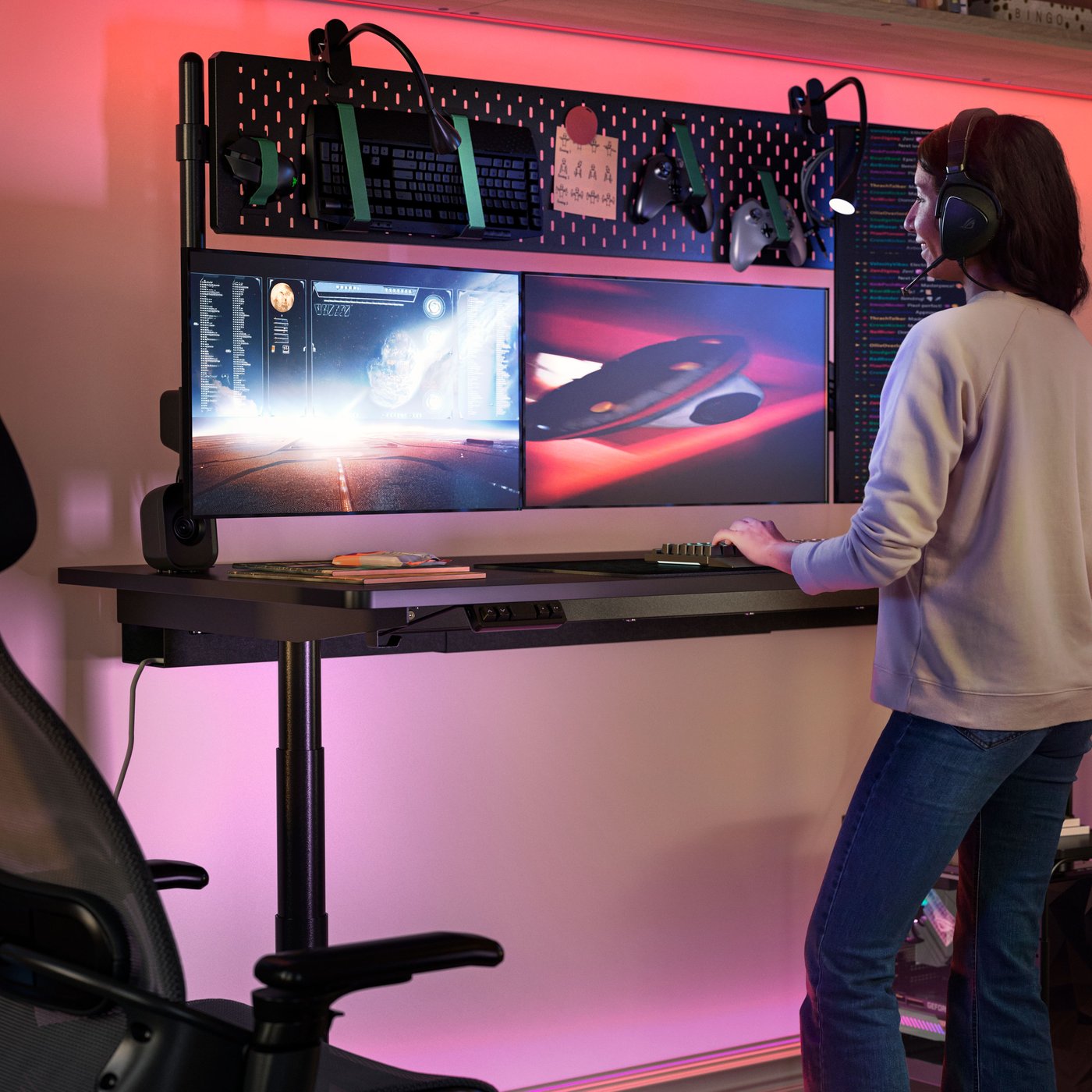 A person is standing at a MÅLOMRÅDE sit/stand gaming desk, playing an online game. Pink light glows behind the desk.