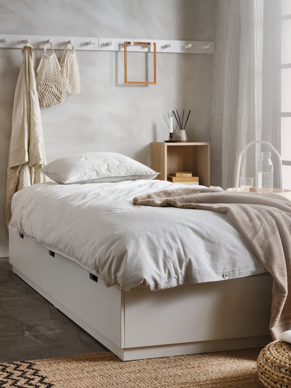 A NORDLI bed with storage with BERGPALM bed linen stands in a bedroom near a NORDKISA open wardrobe with sliding door.