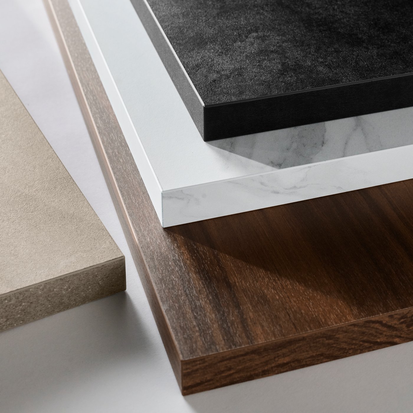 A close up of four IKEA EKBACKEN laminate worktops in grey-beige stone effect, walnut effect, white marble effect and black.