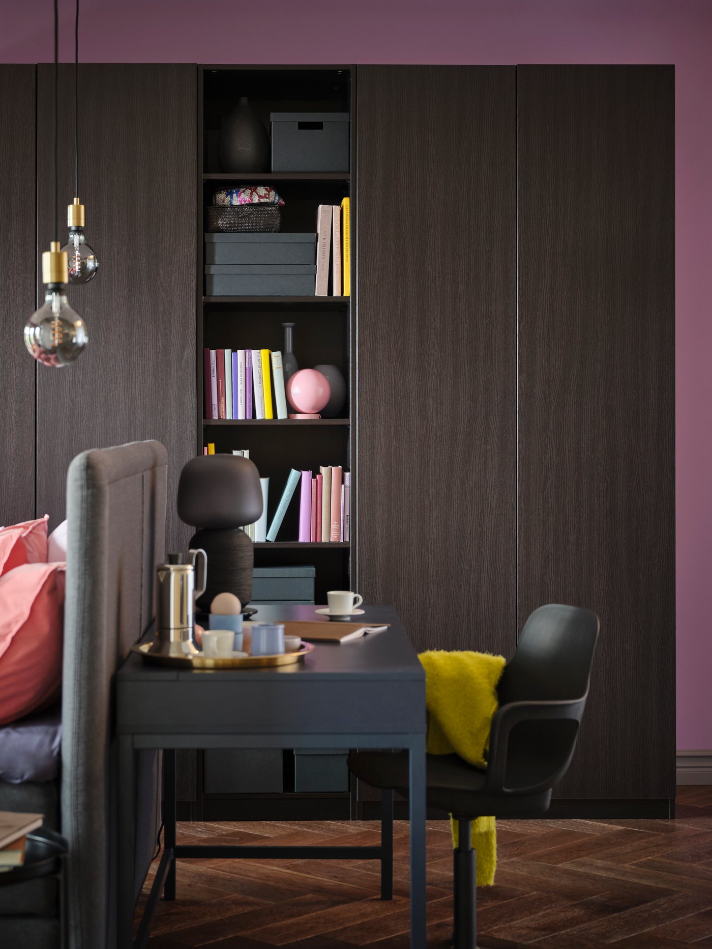 An ALEX desk and an ODGER chair stand in front of a black-brown PAX/FORSAND wardrobe with shelves holding books and boxes.