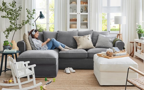 Kvinna som halvligger i en grå GRÖNLID soffa i ljust vardagsrum.