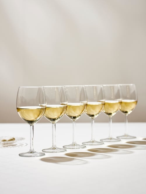 A modern dining room that features a set of six wine glasses in a row on a table covered with a white tablecloth.