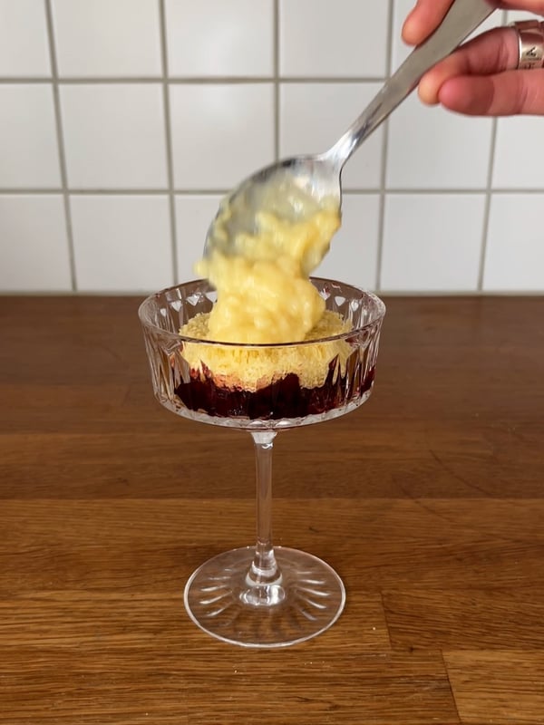 En champagnecoupe med tårtbotten, sylt och vaniljkräm i.