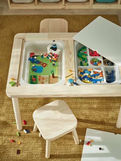 Blick von oben auf einen FLISAT Kindertisch mit einer TROFAST Box, einem TROFAST Aufbewahrungskasten mit Fächern, zwei FLISAT Kinderhockern und einem LANGSTED Teppich.