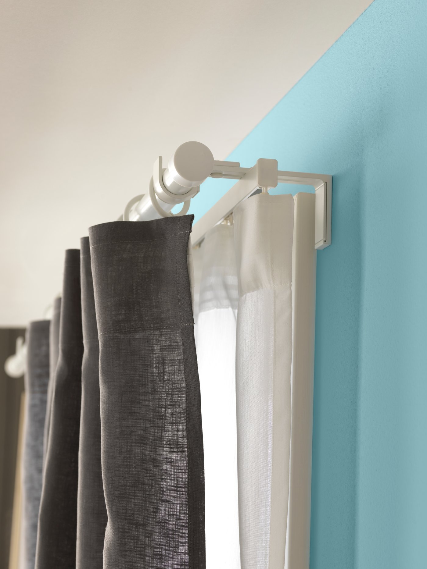 A wall-mounted VIDGA curtain rod with a pair of grey and white curtains. 